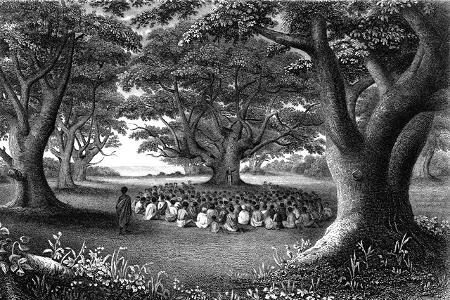 missionary preaching to a crowd sitting under trees