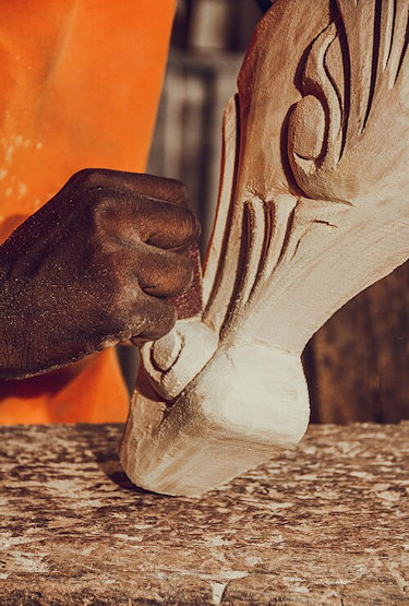 young man's hand carving wooden chair leg