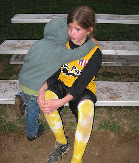 A child with a hurt knee is being comforted by an even smaller child.
